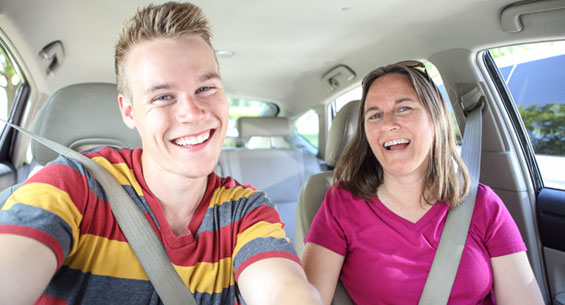 Young man in the driving seat of his parent's car with his mum sitting next to him